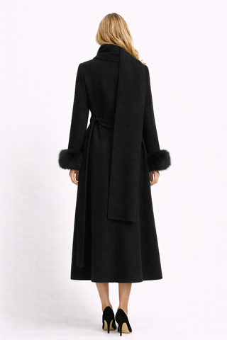 Woman wearing a long black coat with fur cuffs on a white background