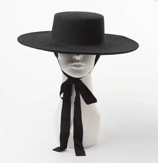 Black wide-brimmed hat with a black ribbon on a white mannequin head against a white background