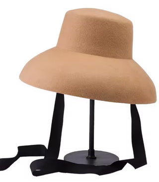 Tan wide-brimmed hat on a black stand against a white background