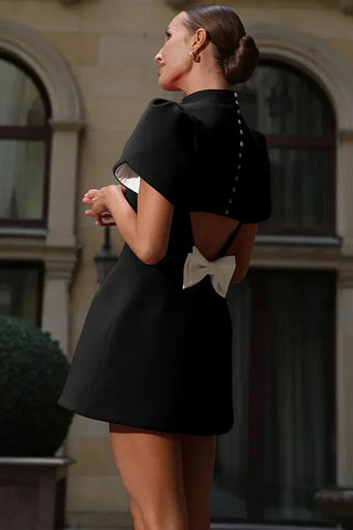 Black mini dress with puff sleeves, pearl back buttons, and white bow