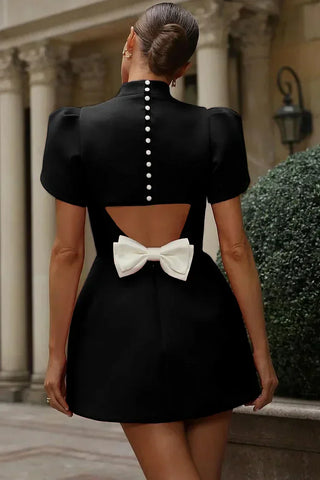 Black mini dress with puff sleeves, pearl back buttons, and white bow