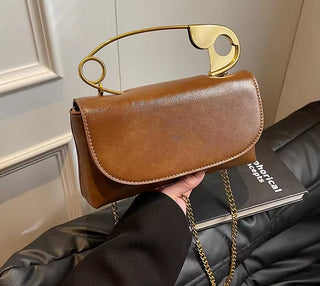 Brown handbag with gold chain held by a person wearing a black coat.
