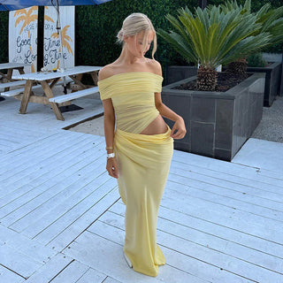 Woman in a yellow off-shoulder dress standing on a wooden deck with plants in the background.