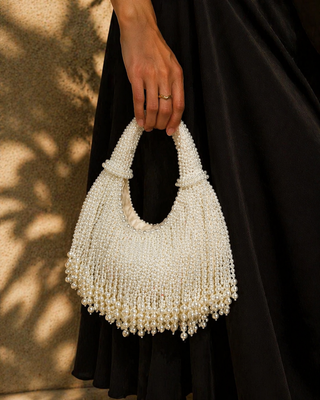 Person holding a white beaded handbag against a black background