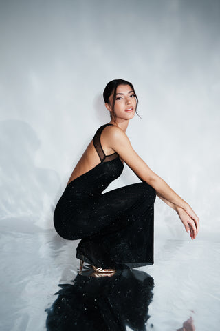 Woman in a black dress sitting on a reflective surface with a white background