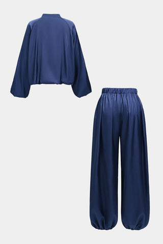 A two-piece navy blue satin-like lounge set consisting of a cropped long-sleeve top with wide draped sleeves and matching wide-leg pants with elastic waistband and gathered cuffs, shown on a light gray background.