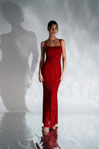 Woman in a red dress standing against a white background with a soft shadow.