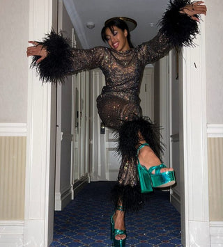 Person in a sparkling outfit with feathered sleeves in a hallway.