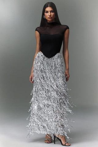 Woman wearing a black top and silver fringe skirt on a gray background