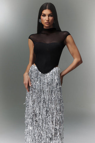 Woman wearing a black sheer top and silver sequin skirt against a gray background