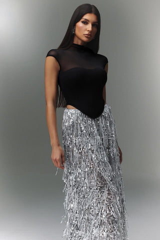 Woman wearing a black top and silver sequin skirt against a gray background