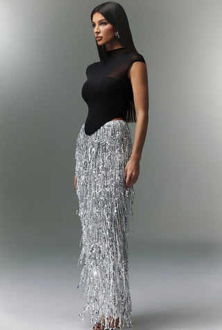 Woman wearing a black top and silver beaded skirt against a gray background