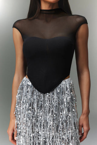 Person wearing a black sheer top and silver sequin skirt on a gray background