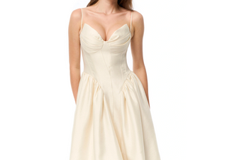 A woman wearing a cream-colored corset-style dress with thin spaghetti straps, a structured bodice, and a voluminous skirt, shown against a plain white background.