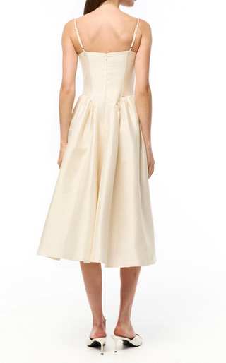 A woman shown from the back wearing a cream-colored sleeveless midi dress with thin straps, a structured corset-style bodice, and a flared skirt, paired with white mule heels on a white studio background.