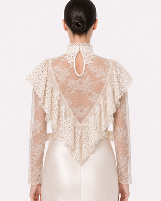 Back view of a model wearing a cream lace long-sleeve top with a high keyhole back and a satin skirt against a plain white background.