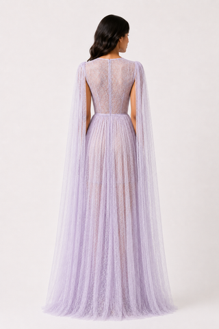 A model shown from the back wearing a lavender tulle gown with a sheer lace back and long draped cape sleeves, photographed against a plain light background.