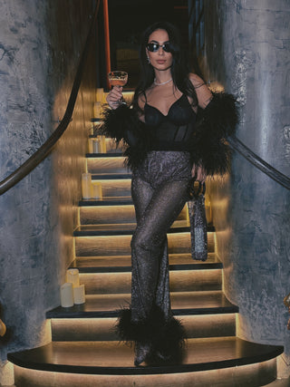 Woman in glamorous outfit with fur and sequin pants standing on a staircase holding a drink.