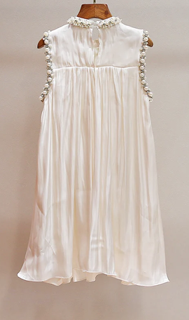 An off-white satin nightgown with pearl embellishments along the neckline and armholes, displayed on a wooden hanger against a neutral beige background.