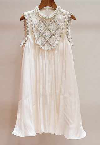 An off-white sleeveless dress with intricate pearl and bead embellishments around the neckline and shoulders, hanging on a wooden hanger against a plain beige background.