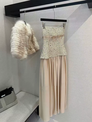 A two-piece women's outfit displayed on hangers against a light gray wall. The set includes a strapless tweed mini dress with a pleated beige skirt and a fluffy cream faux-fur cropped jacket hanging beside it.