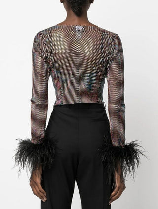 Person wearing a sheer top with feather details and black pants on a white background