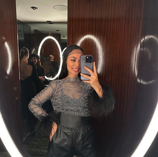 Person taking a mirror selfie wearing a sparkly top and black pants in a room with wooden walls.