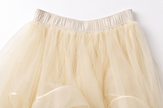 A close-up of a cream or pale beige tulle skirt with a gathered elastic waistband, shown against a plain white background.