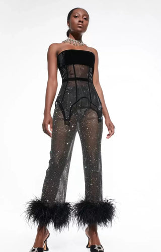 Model wearing a black sheer jumpsuit with feathered cuffs on a white background