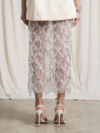 Person wearing a sheer beaded skirt with white high-heeled shoes against a neutral background