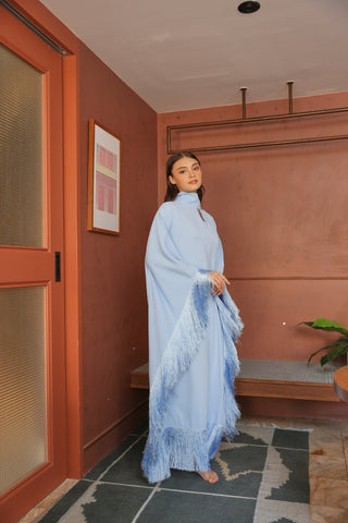Woman in a light blue dress standing in a room with pink walls and a plant.