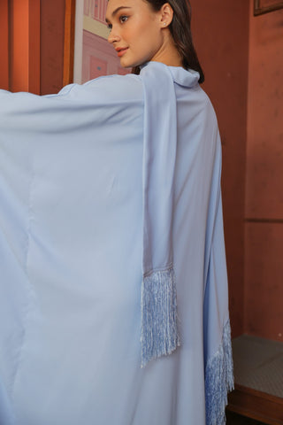 Woman wearing a light blue shawl with fringe details against a pink wall.