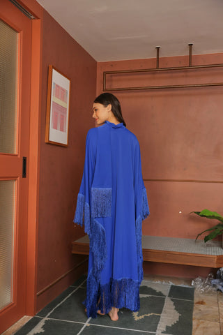 Woman in a blue dress standing in a room with a red wall and wooden door.