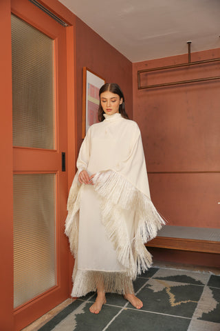 Woman in a white dress with fringe standing in a room with a red wall and wooden door.