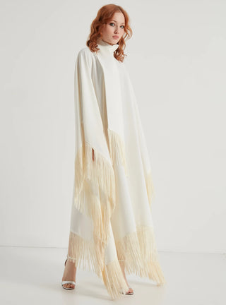 Woman wearing a long, light-colored dress with fringe details on a white background