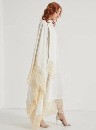 Woman wearing a long, light-colored dress with a sheer overlay against a white background