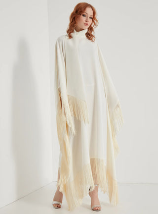 Woman wearing a long, light-colored dress with fringe details against a white background
