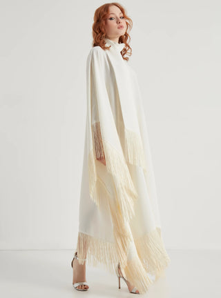 Woman wearing a long, light-colored dress with fringe details on a white background