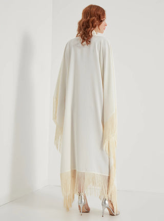 Woman wearing a long, light-colored shawl with fringe details on a white background