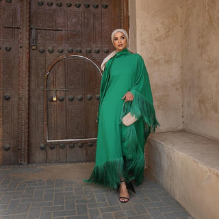Woman in a green dress with fringe standing in front of a wooden door.