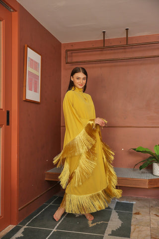 Woman in a yellow fringed dress standing in a room with red walls and a plant.