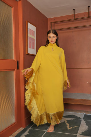 Woman in a yellow dress standing in a room with a red wall and framed picture.