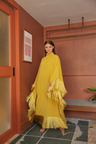 Woman in a yellow dress standing in a room with a red wall and a plant.