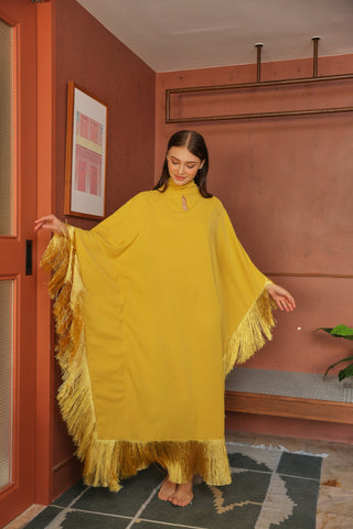 Woman wearing a yellow fringed dress in a room with pink walls and a plant.