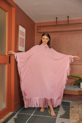 Woman in a pink dress with fringe standing in a room with a red wall and a plant.