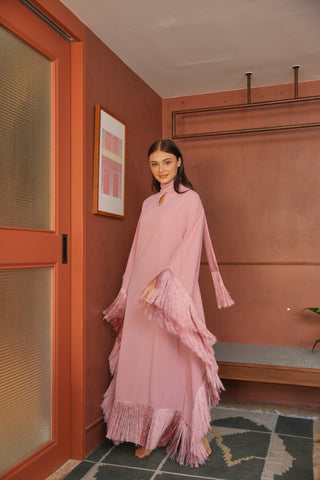 Woman in a pink dress standing in a room with a red door and wall. Fringe Tassel Dress