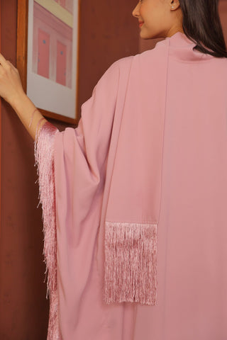 Person wearing a pink outfit with fringe details, standing against a red wall.