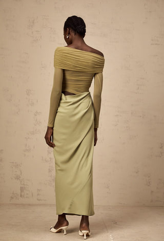 Woman wearing a green off-shoulder dress against a beige wall.
