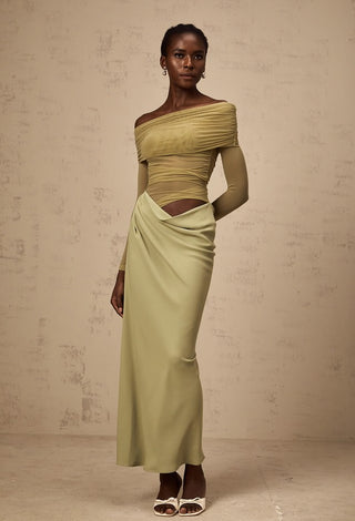 Woman wearing a green off-shoulder top and skirt against a beige background