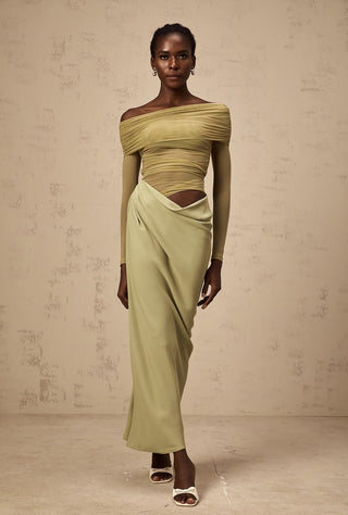 Woman wearing a green off-shoulder top and skirt against a beige background